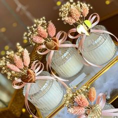 three glass vases with pink flowers and bows on them sitting on a gold stand