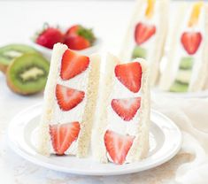 two slices of cake with strawberries on top and kiwis in the background