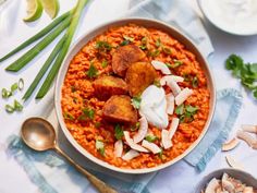 a bowl filled with rice and meat on top of a blue table cloth next to spoons