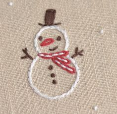 a close up of a snowman embroidered on a piece of fabric with white and red thread