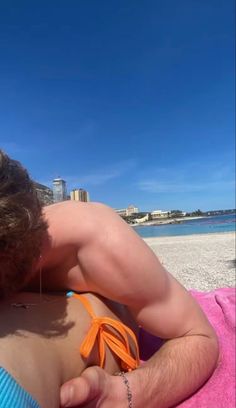 a man laying on top of a pink towel next to the ocean with his back turned