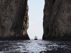 a boat is in the water between two large rock formations, with one person on a small boat