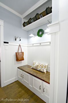 a wooden bench sitting in the middle of a room next to white cabinets and drawers