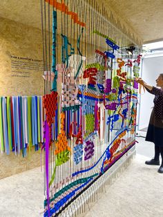 a woman standing next to a wall covered in lots of different colored beads and wires