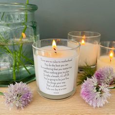 some candles are sitting on a table next to flowers and glass vases with plants in them