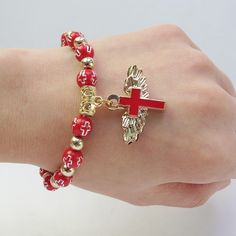 a woman's hand with a red cross and gold beads bracelet on her wrist