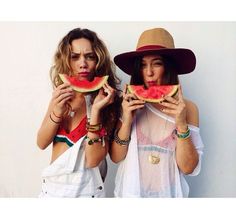 two women holding slices of watermelon in front of their faces while posing for the camera