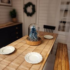 a wooden table topped with plates and a snow globe filled with a blue christmas tree