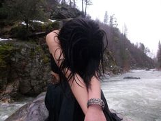 a woman sitting on top of a rock next to a river