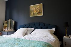 a bed with white pillows and blue headboard in a bedroom next to a painting on the wall