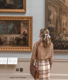 a woman standing in front of some paintings and holding a purse with her hand on her hip