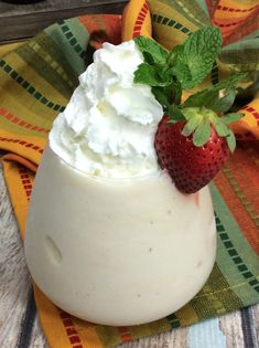 a strawberry and whipped cream dessert in a glass on a colorful cloth with a green leaf