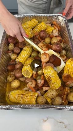 a person cutting up some food on top of a metal pan filled with potatoes and corn