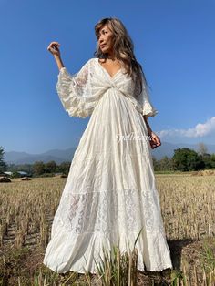 a woman standing in a field wearing a white dress and holding her hand out to the side