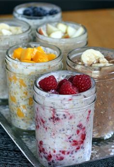 four jars filled with different types of food on a tray next to bananas and raspberries