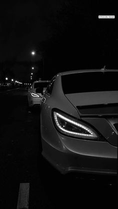 two cars parked in a parking lot at night with the headlights turned on and no people around