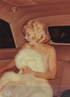 a woman sitting in the back seat of a car with a fur stole around her neck