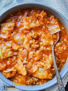 a bowl full of cabbage and meat soup with a spoon next to it on a towel