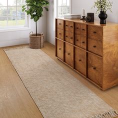 a wooden dresser sitting next to a window in a room with white walls and wood floors