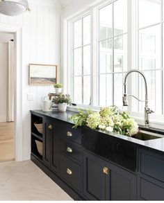 a kitchen with black cabinets and white flowers on the counter top next to a window