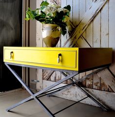 a vase with flowers sitting on top of a yellow table next to a wooden door