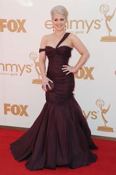 a woman in a purple dress standing on a red carpet with her hands on her hips