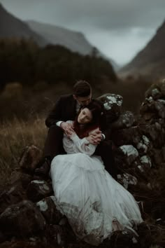 a bride and groom sitting on rocks in the mountains