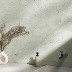 a white vase with dried plants in it next to a faucet and soap dispenser