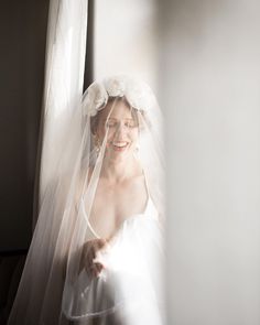 a woman in a wedding dress standing next to a window with a veil on her head