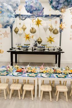 a table set up for a party with paper stars on the ceiling and plates in front of it