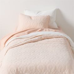 an unmade bed with peach colored sheets and pillows on top of it, in front of a white wall