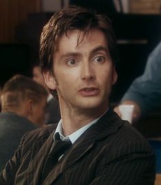 a man in a suit and tie sitting at a table with other people behind him