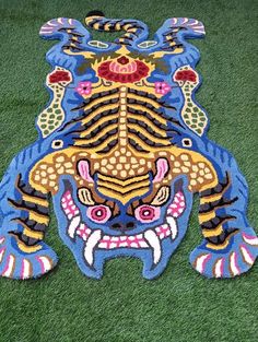 an animal rug is on the ground with green grass in front of it and blue, yellow, red, and orange colors