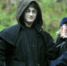 a young man wearing glasses and a hooded jacket is walking in the rain with other people behind him