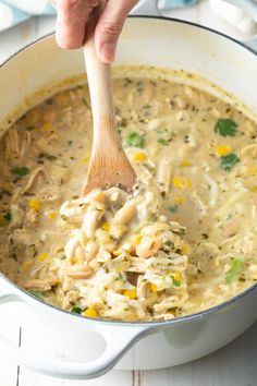 a wooden spoon in a white pot filled with chicken and rice casserole soup