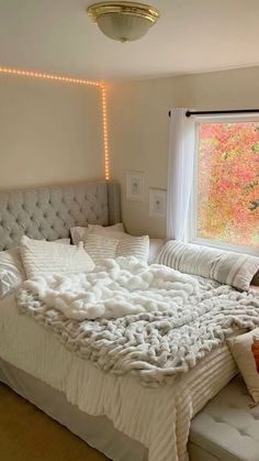 a large bed sitting in a bedroom next to a window covered in blankets and pillows