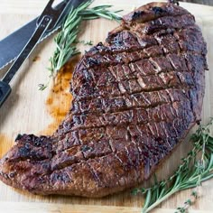 a piece of steak on a cutting board next to a pair of tongs and a knife