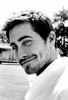 a black and white photo of a man smiling at the camera with trees in the background