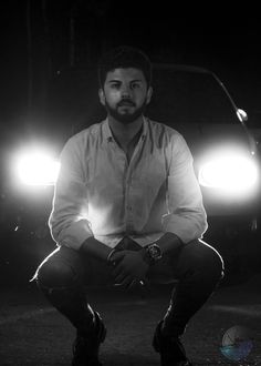 a man sitting on the ground in front of a car at night with two headlights