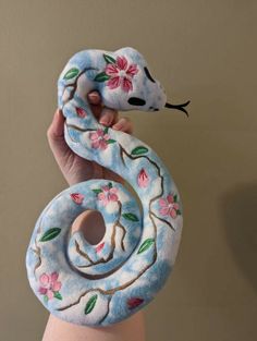 a hand holding up a stuffed animal snake with flowers on it's body and tail