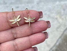 Materials: * 18 kt Gold Plated Dragonfly Charms * Cubic Zirconia  * 14 kt Gold Filled Ear Wires Dainty Gold Dragonfly Dangle Earrings with 14kt gold filled ear wires. The Dragonfly Charms are a long lasting 18kt gold plate with a single Cubic Zirconia stone for a bit of sparkle. They will remain bright, shiny and tarnish free with proper care. The ear wires are 14 kt gold filled and are great for sensitive ears! They come complete rubber backings so you will never have to worry about losing these beautiful, lightweight earrings. These earrings come to you in a lovely gift box ready for gift giving. I also make a beautiful matching necklace which can be seen in the last picture of this listing and the link for it is below: Necklace:  https://www.etsy.com/listing/726526401 These beautiful, l Dragonfly Jewelry, Dragonfly Charm, Dragonfly Earrings, Summer Earring, Red Earrings, Butterfly Necklace, Light Weight Earrings, Matching Necklaces, Summer Jewelry