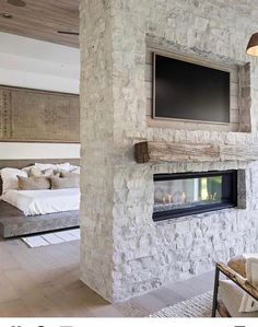 a stone fireplace with a flat screen tv above it in a living room next to a bed