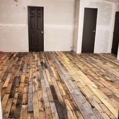 an empty room with wooden floors and two black doors in the center is painted white