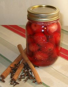 a jar filled with lots of red apples next to cinnamon sticks