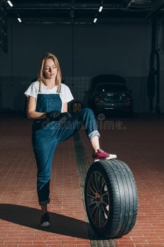 a woman in overalls is sitting on top of a tire