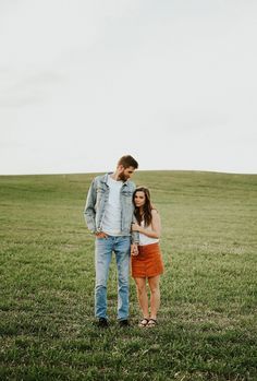 a man and woman standing in the middle of an open field with grass on both sides