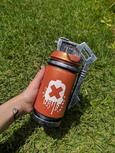 a hand holding an orange and black water bottle on top of green grass with a wrench attached to it