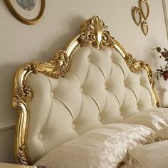 a white bed with gold trimmings in a bedroom next to a mirror and flowers