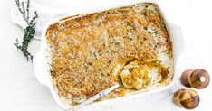 a casserole dish with potatoes and parmesan cheese on top, next to two wooden utensils