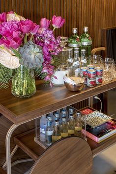 a wooden table topped with lots of bottles and glasses next to a vase filled with flowers